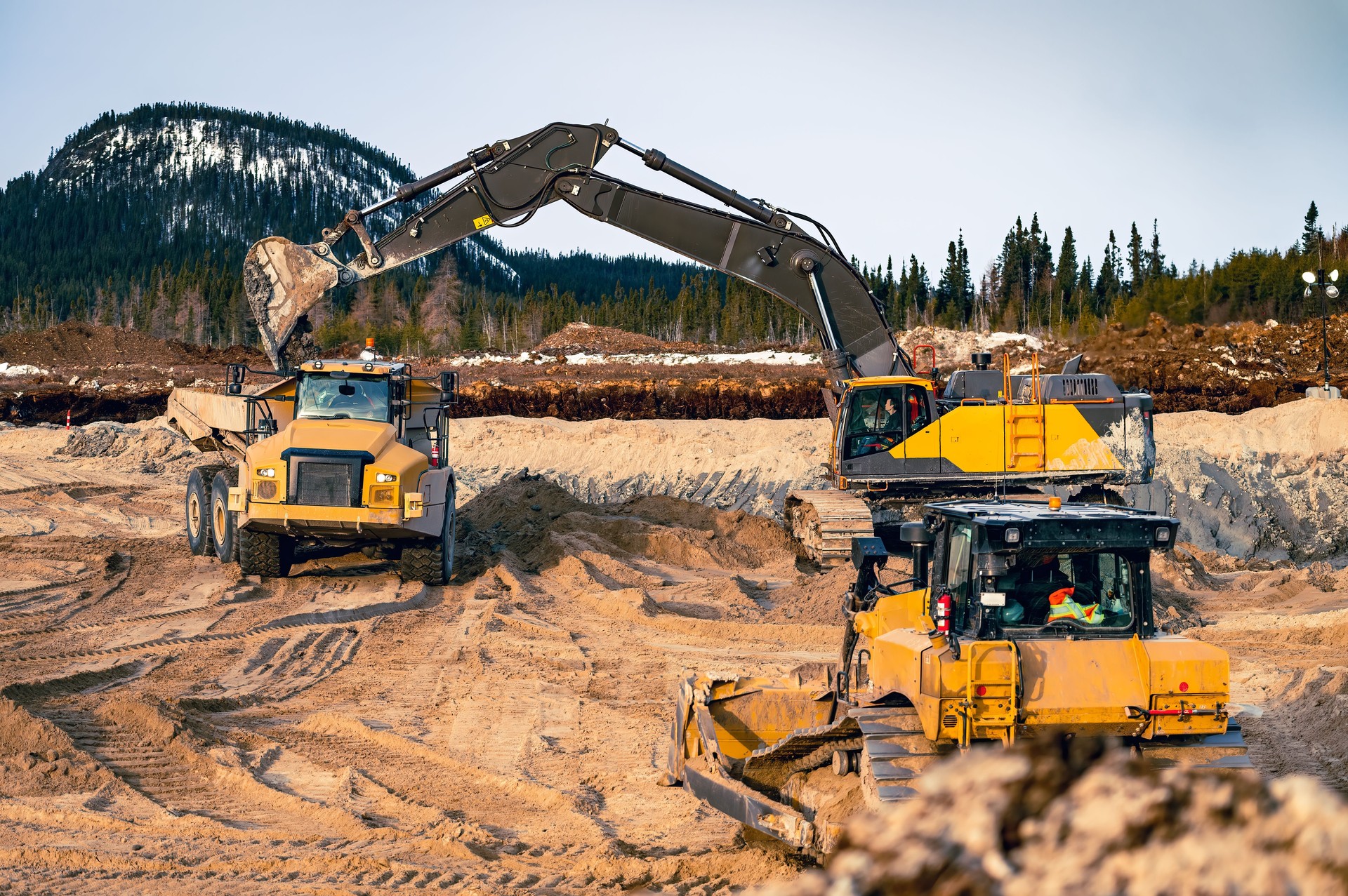 Excavator loading a dump truck with topsoil and with an approaching bulldozer